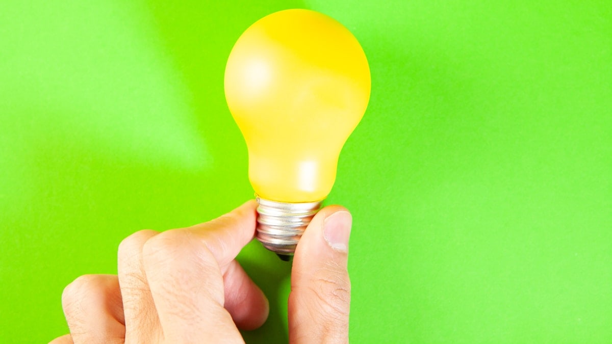 Yellow light bulb in hand on a green background. The concept of saving energy
